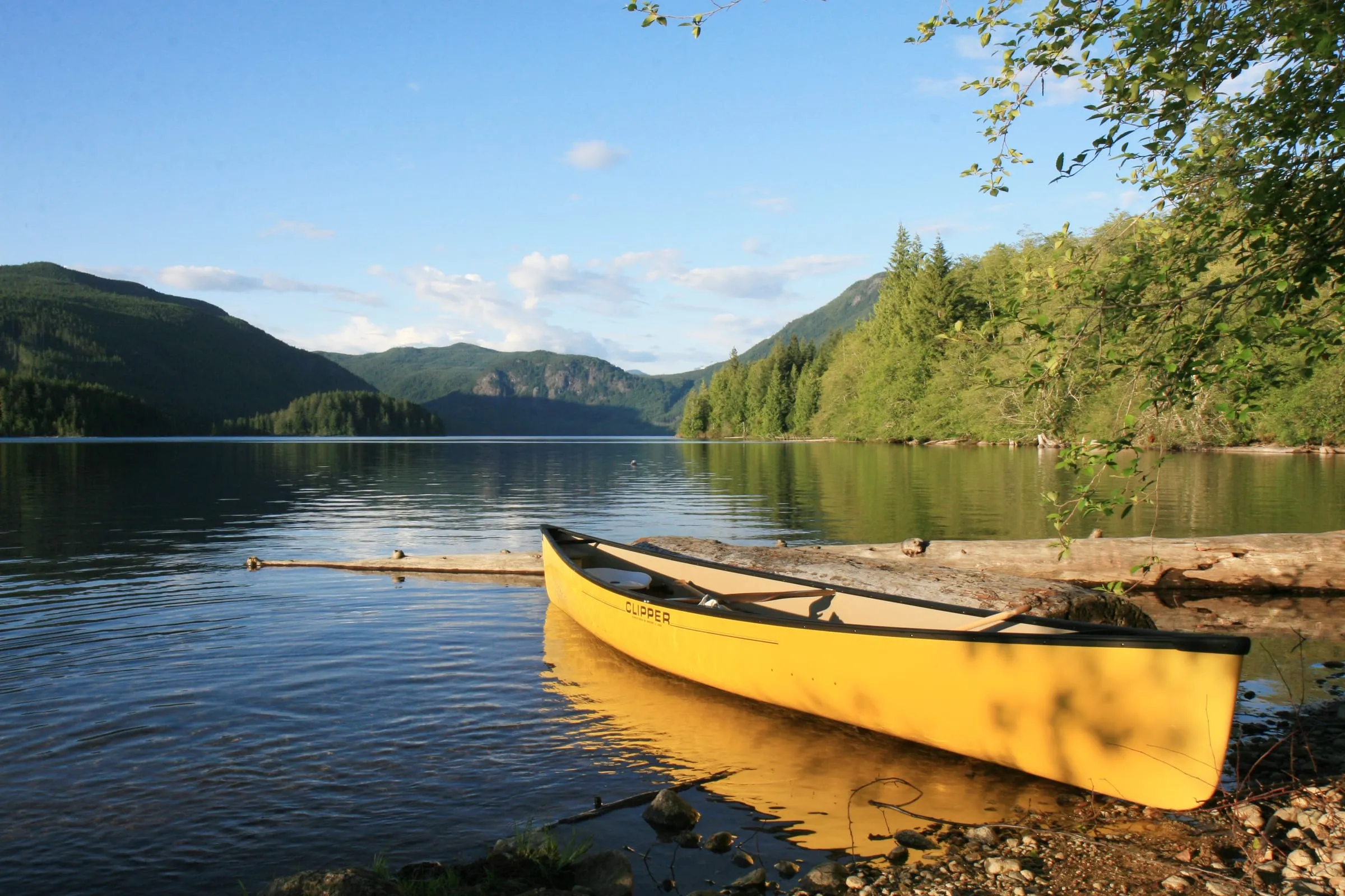 A canoe resting at the edge of a calm lake ringed by hills