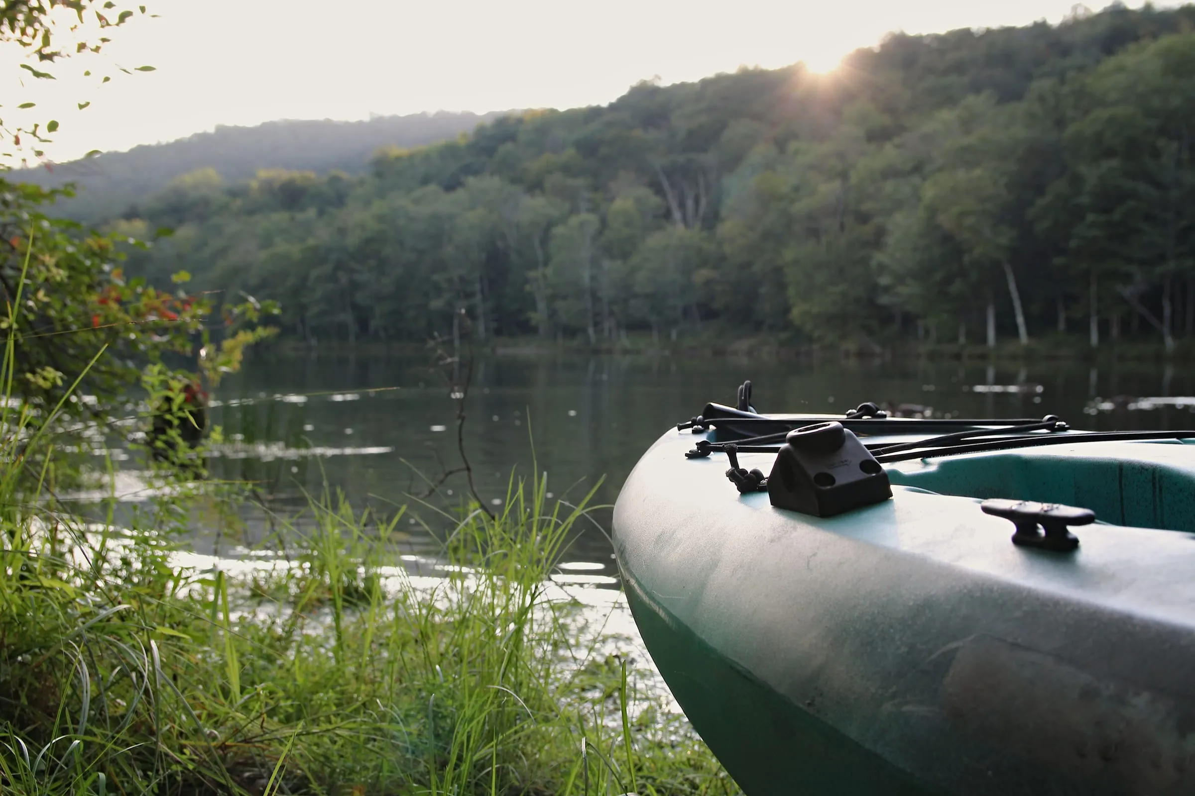 A kayak resting on a quiet, tree-lined Catskills lakeshore at golden hour