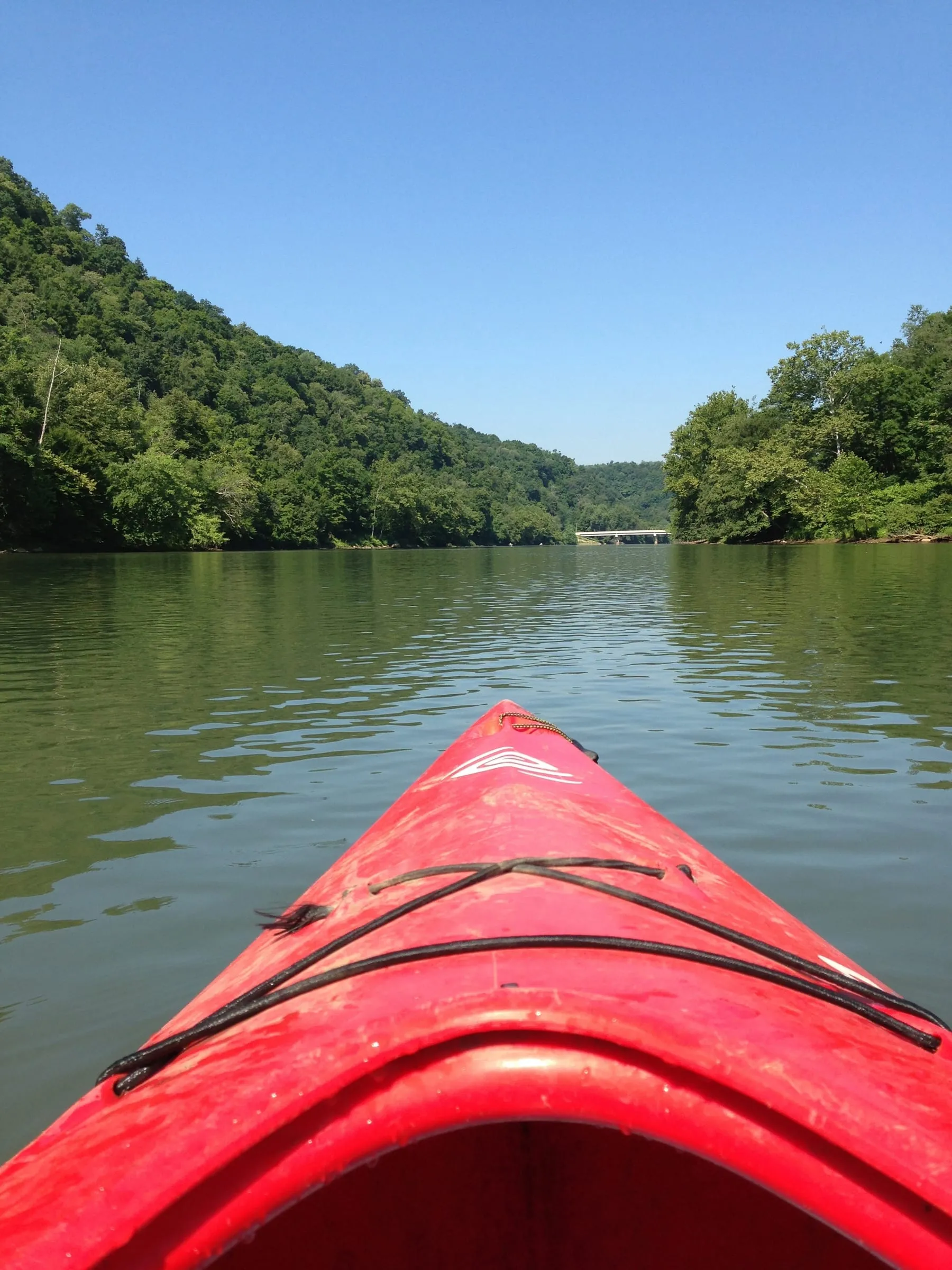 First-person view from a kayak on calm water under a clear blue sky