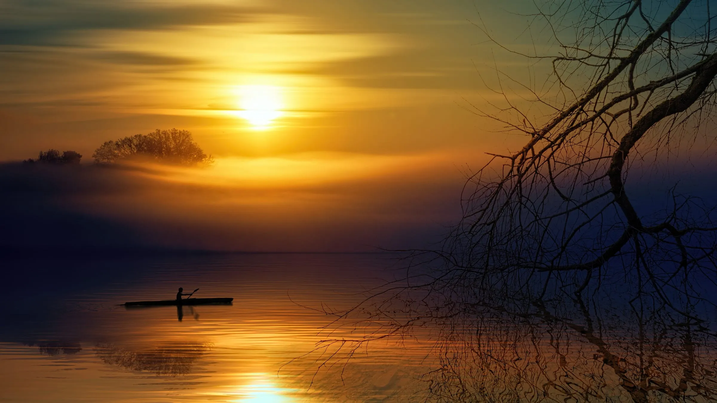 A lone paddler on calm, misty water at sunset